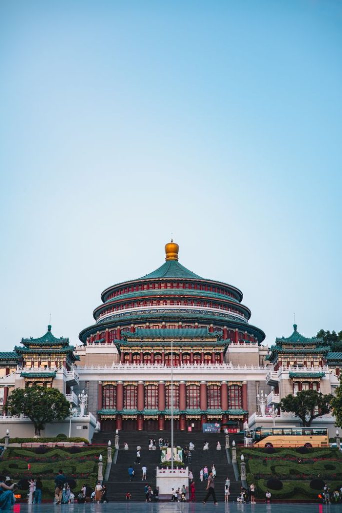 View of Chongqing People's Great Hall under a clear sky at dusk with scattered visitors.